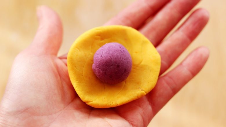 南瓜水晶紫薯包,用手摁扁后，把静置好的紫薯揉成圆球放到南瓜面皮上面。