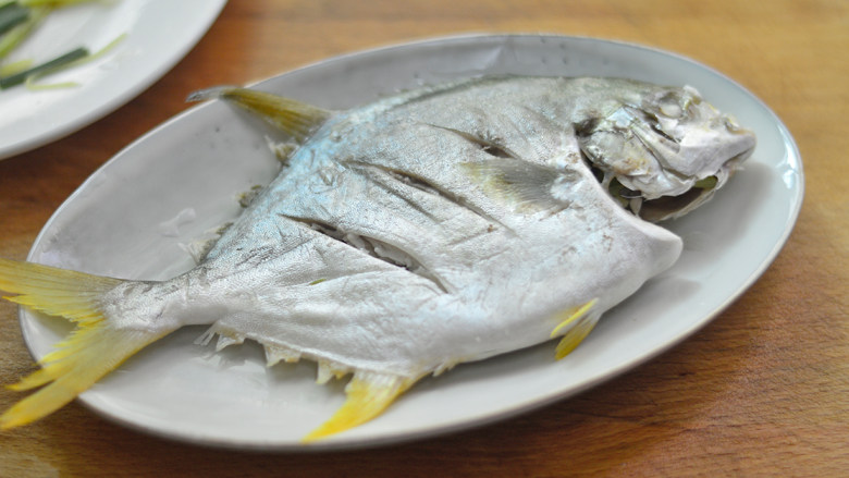 清蒸金鲳鱼,夹去姜丝和葱段，摆入干净的盘子里