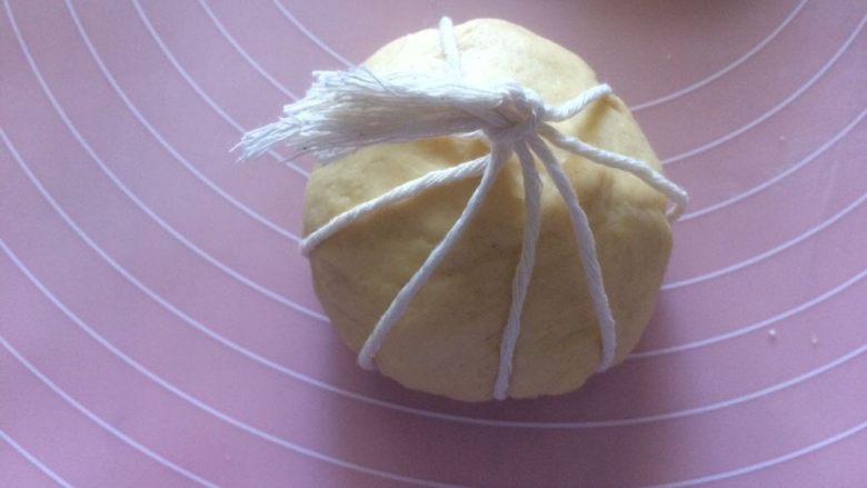 金灿灿的黄金南瓜面包,轻轻地把面团放到米字正中间的交叉点，依次把每根棉线提起来，捏在手里面，最后打一个结，中间留出一定距离，二发会膨胀；