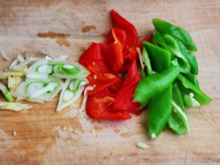 双椒爆鸡块,把青红尖椒洗净后用用刀切成薄片，葱姜切丝备用。