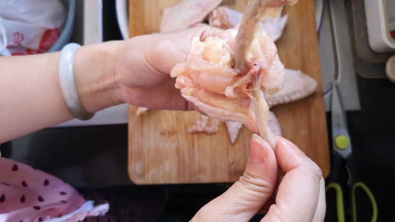 奥尔良鸡翅包饭,筋剪断后，将肉往下退，两根骨头很容易就掰离开了，如图所示。