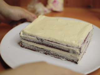 红丝绒蛋糕 无需酪乳 奶酪霜抹面,裱花袋剪1cm的口子，奶酪霜覆盖整片蛋糕。
用抹刀抹平，盖上另一片蛋糕。
同样盖上奶酪霜，抹匀。
侧面先不要全部覆盖，薄薄得抹匀就可以了，把奶酪霜和蛋糕都放入冰箱冷藏1小时以上。
这样涂抹一遍，冷藏凝固，再抹奶油不容易把蛋糕屑带出来。
