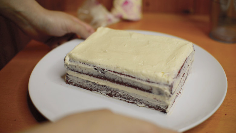 红丝绒蛋糕 无需酪乳 奶酪霜抹面,裱花袋剪1cm的口子，奶酪霜覆盖整片蛋糕。
用抹刀抹平，盖上另一片蛋糕。
同样盖上奶酪霜，抹匀。
侧面先不要全部覆盖，薄薄得抹匀就可以了，把奶酪霜和蛋糕都放入冰箱冷藏1小时以上。
这样涂抹一遍，冷藏凝固，再抹奶油不容易把蛋糕屑带出来。