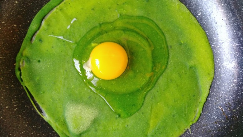 菠菜煎饼果子,在上面放一个生鸡蛋。戳碎，平摊到面饼上。