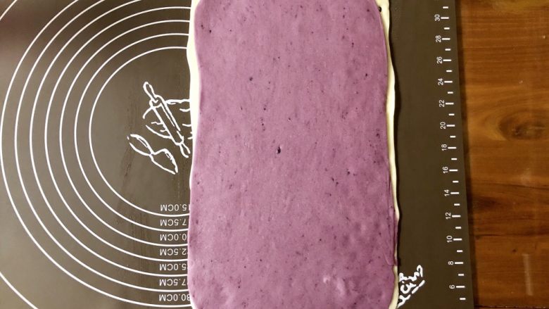 小清新紫薯馒头卷,然后在白色面片上喷一些水，把紫色面片叠上去，用擀面杖轻轻擀一擀，让两张面皮粘合在一起。