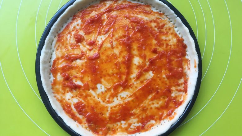 黑椒牛肉肠披萨,用刮刀抹上一层番茄酱
