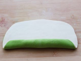 菠菜双色花样小馒头卷,然后在绿色的面片上抹一点水，把白色的面片放在上面，用擀面杖轻轻擀一擀，让两张面皮粘合在一起，然后从没有孔的地方开始卷起。