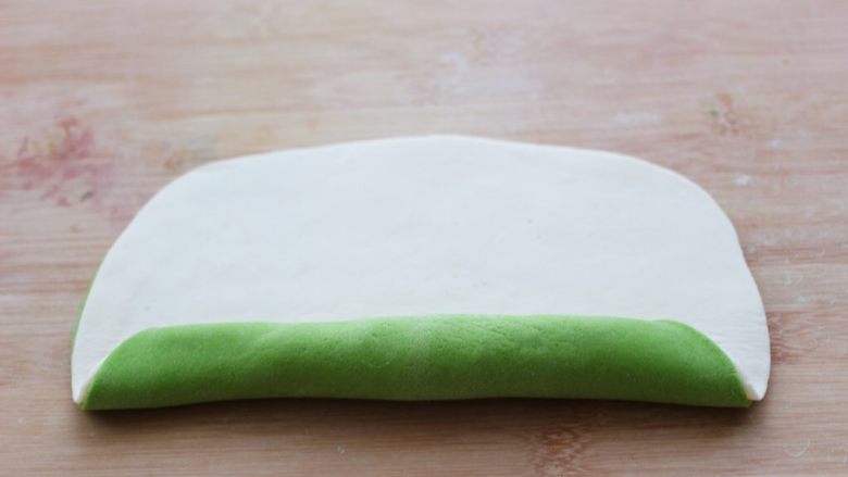 菠菜双色花样小馒头卷,然后在绿色的面片上抹一点水，把白色的面片放在上面，用擀面杖轻轻擀一擀，让两张面皮粘合在一起，然后从没有孔的地方开始卷起。