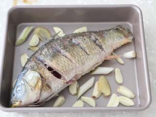 香辣烤鱼,烤盘底部铺上蒜瓣、姜片、葱段，将煎好的鱼放入烤盘中。