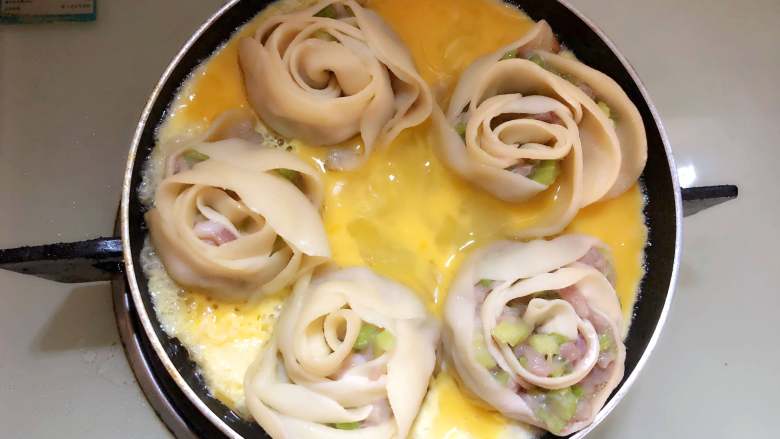 玫瑰花抱蛋煎饺,倒入平底锅里，盖上盖子，继续煎至蛋液完全凝固。