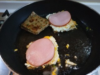 新文美食  葱油饼沾鸡蛋加肠片,把火腿片放在鸡蛋上。在盖上一块葱油饼