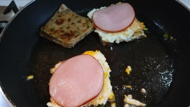 新文美食  葱油饼沾鸡蛋加肠片,把火腿片放在鸡蛋上。在盖上一块葱油饼