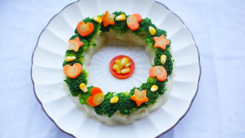 西兰花土豆泥版的圣诞花环,西兰花上摆上处理好的胡萝卜和玉米粒装饰。
圣诞花环，代表了一种保护和庇佑，可以让宝宝们在新的一年中不受妖魔伤害。