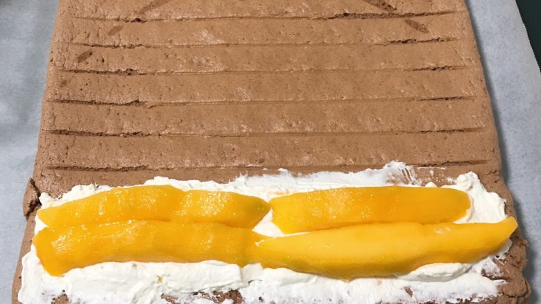 芒果蛋糕卷,蛋糕有余热的时候，均匀的涂抹奶油霜，再放入芒果条。