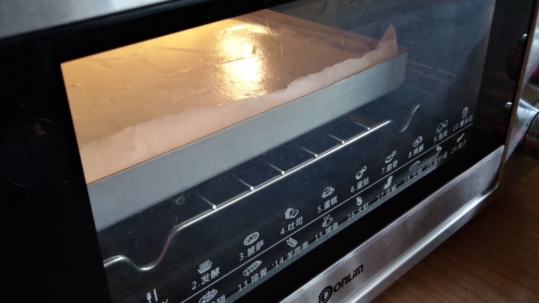 圣诞树根蛋糕,倒入铺了油纸的正方形烤盘里，在桌面上震几下，震出气泡，放入已经预热好上火170度下火175度的东菱烤箱，中下层烘烤18分钟左右