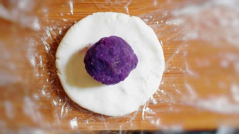 紫薯山药糯米饼（微笑饼）,取一个剂子，用手压成饼状，并取一个紫薯泥团子，放在饼上。