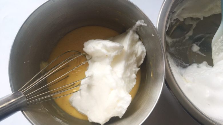 依云米奇蛋糕卷,冰箱取出冷藏的蛋白霜，先取一部分蛋白霜加入到蛋黄糊中，用蛋抽翻拌均匀
