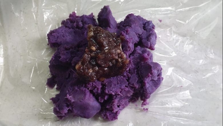 颜色艳丽的紫薯茶巾绞，给餐桌上加点不一样的色彩,取一小块的紫薯泥，放在保鲜膜上，压平加入适量的红豆沙
