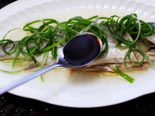 鲜美无比的粤式清蒸鲈鱼,沿着盘子的四周浇上蒸鱼豉油。