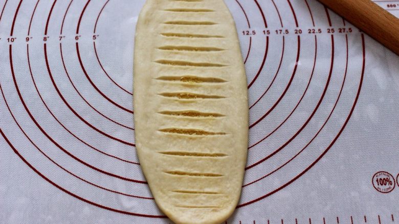 椰蓉奶香面包圈,用锋利的刀片在面团表面均匀的割几刀，注意只切透上面一层即可。（擀的时候用力要均匀，否则容易将椰蓉馅挤出）