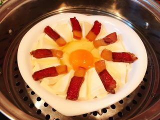 腊肉蒸豆腐卧蛋,摆好盘的腊肉豆腐鸡蛋装入蒸锅蒸大火蒸十五分钟