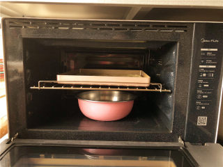 香葱肉松面包卷,把烤盘放到烤箱里，下方放一盆热水二次发酵。一般温度在35度-40度之间，二次发酵时间约30-40分钟。
