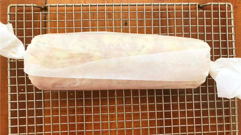 香葱肉松面包卷,趁着余热把面包卷起来，用油纸包裹之后拧紧两边固定一下，放凉以后再打开。
