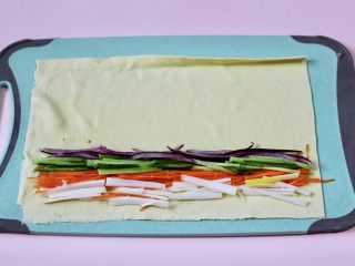 经典不衰的京酱肉丝,把焯过水的豆腐皮铺平后，放入提前切丝的黄瓜和胡萝卜，大葱和洋葱丝。