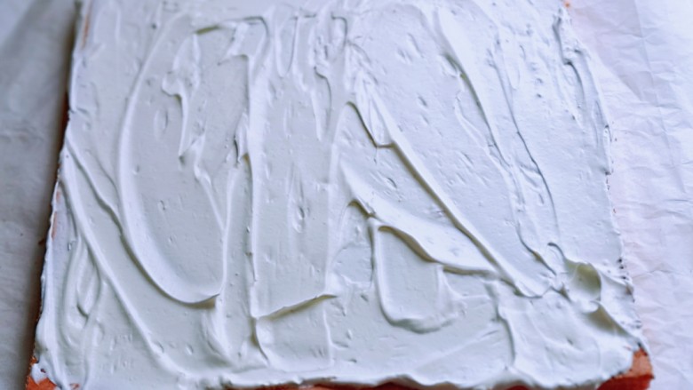 红丝绒草莓奶油蛋糕卷～下午茶必备甜品,将蛋糕片放一张油纸上面，打发的奶油涂抹在蛋糕片上。借助擀面杖和油纸从一段卷起来即可，放入冰箱冷藏1小时以上再切开。(奶油留一些，做装饰用)