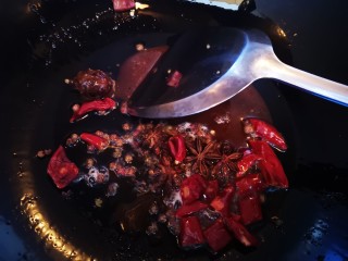 秘制红烧牛肉,待白糖融化后加入干辣椒段、八角和花椒粒炒香
