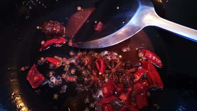 秘制红烧牛肉,待白糖融化后加入干辣椒段、八角和花椒粒炒香