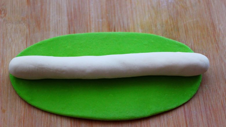 双色金鱼花样馒头,把绿色的面团搓成长条后压扁，用擀面杖擀成椭圆形，再把白色面团搓成长条，放在绿色面皮上。