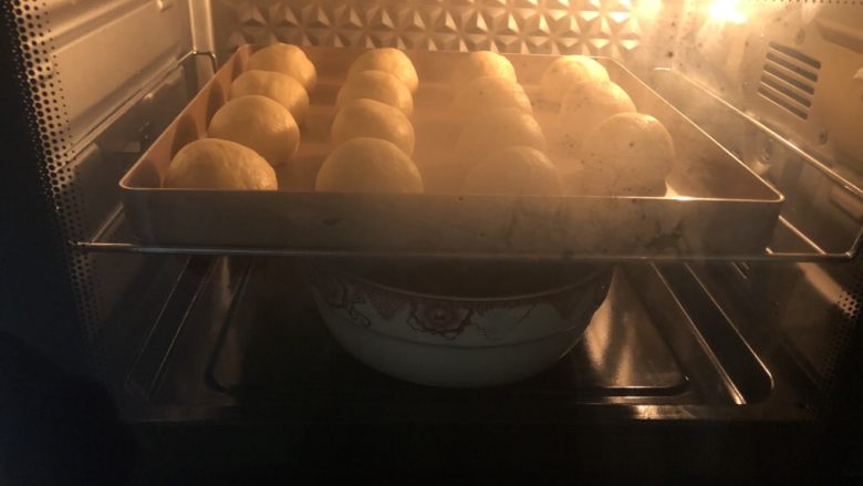椰蓉小餐包,把烤盘放入烤箱里利用烤箱自动发酵功能把面团发酵成原来的1.5到2倍大，在下面或者旁边放一盘热水，保证面团的湿度和温度。