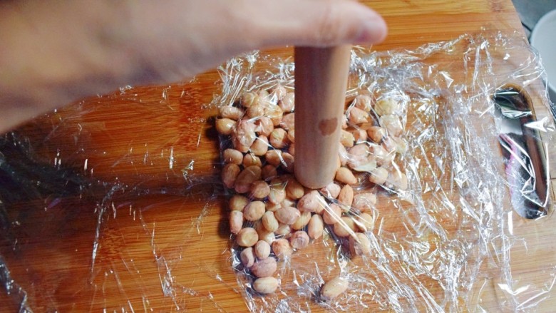 紫薯南瓜糯米糕,将晾干的花生米用保鲜膜包起来，并用擀面杖捣碎，去除比较容易去的花生皮（也可不去）。