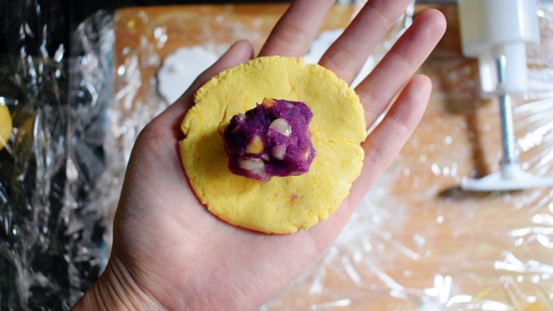 紫薯南瓜糯米糕,取一个面剂子，用手压成圆形，放一个紫薯花生丸。