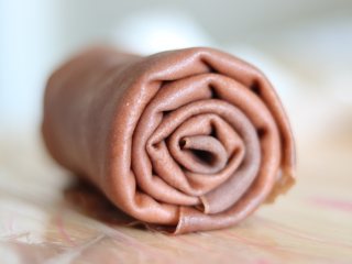巧克力毛巾卷,两手把它卷起来，卷的时候，稍微卷紧实一些，之后包好保鲜膜冷藏定型。