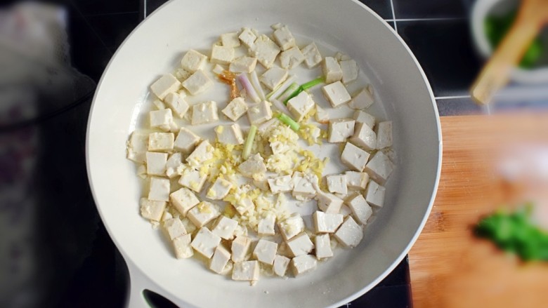 金钩海米炒豆腐,煎至微黄时，加入葱段、姜末和蒜末。