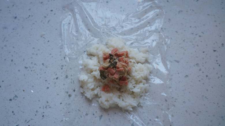 小猪饭团,保鲜膜刷一层食用油，铺上适量米饭，放一勺香肠肉松，借助保鲜膜做成饭团。