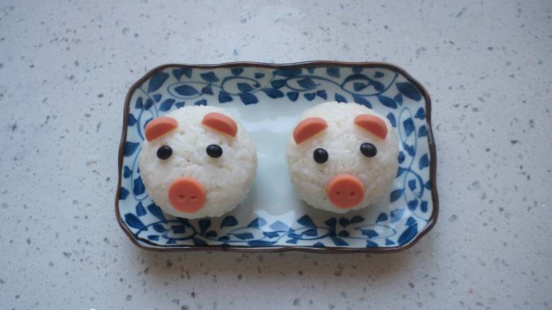 小猪饭团,再用之前准备好的香肠装饰成小猪的样子。眼睛我是用的黑豆。也可以用海苔剪成圆形来装饰。