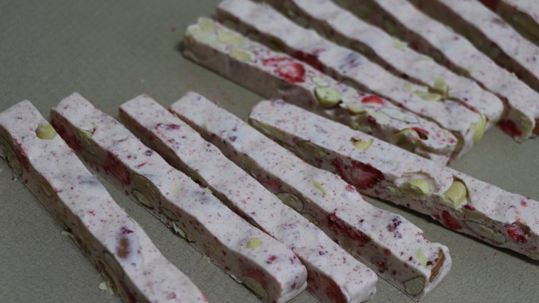 草莓牛轧糖，酸甜美味新年糖,利用方木条，比着把糖切出长条。