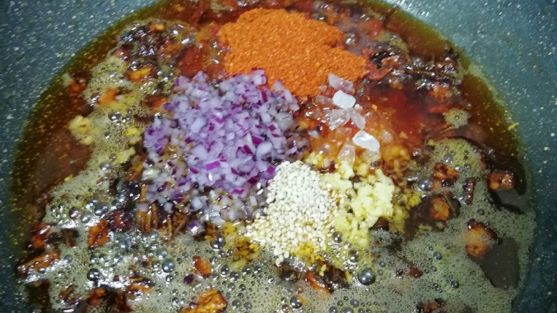 菌菇素辣酱,放入白芝麻、辣椒粉、冰糖碎、洋葱碎末和生姜碎末，转小火炒至辣椒出红油。