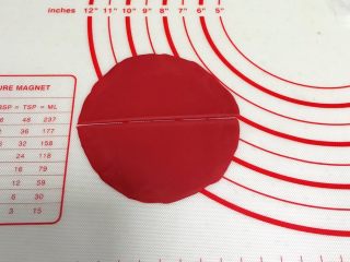 小福猪中国结馒头,取12克红色面团，揉匀排气滚圆，擀成圆形薄片，中间一切为二。