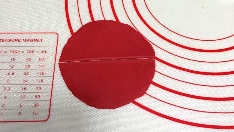 小福猪中国结馒头,取12克红色面团，揉匀排气滚圆，擀成圆形薄片，中间一切为二。