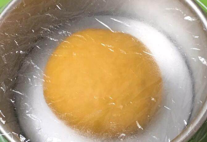 南瓜豆沙味喜饼,厨师机揉面至面粉结团，无需出膜状态。揉面完成整理、滚圆放入模具，盖上保鲜膜。