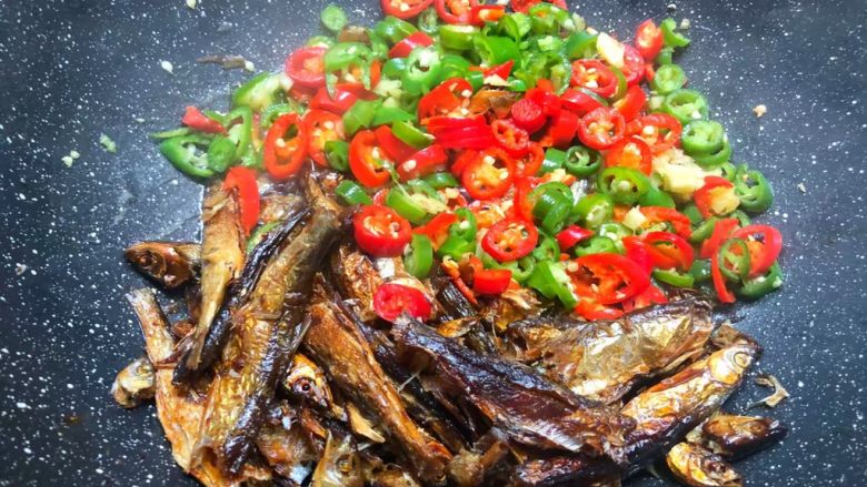 辣炒溪鱼干,溪鱼干炸好以后，把鱼干拨到一边，把生姜末和青红辣椒放入炒至断生。