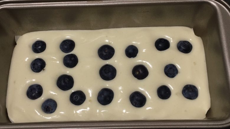 蓝莓玉枕蛋糕,吐司盒中放一张烤盘纸，方便脱模，蛋糕糊倒入模具一半，放入蓝莓。