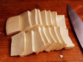 香辣煎豆腐,把北豆腐用水冲一下后，用刀切成0.5厘米的薄片，也可以根据自家的需求增减豆腐的量。
