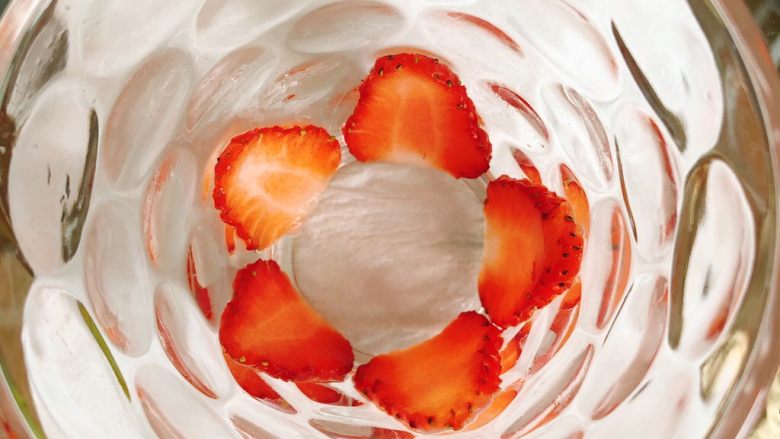 草莓奶昔,取2个差不多大小的草莓对半切开，再切成薄片贴在透明杯子底部。
