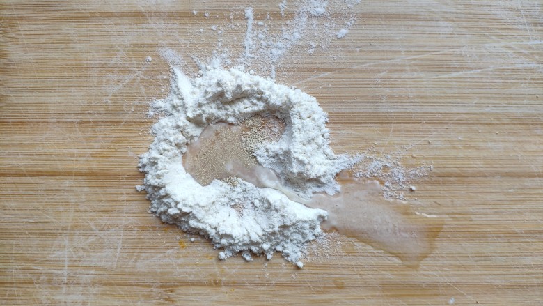 土豆造型豆沙包(馒头),取5—10克面粉放在面板上，加入一点点酵母，倒入少许水，和成一块小的白面团。(用来制做土豆芽)