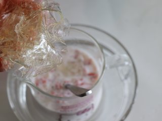 自制健康美味的草莓牛奶果冻,泡软的吉利丁片挤干水分，放到杯中，搅匀使其融化。